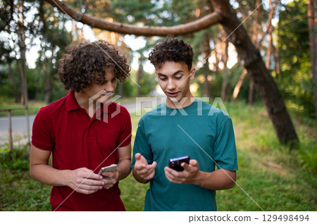Teens with phones in hands spending time together in the park Teens with phones in hands spending time together in the park 129498494