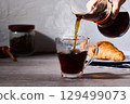 A breakfast scene with croissants and hot coffee poured in. A cafe-style image with white walls and a wooden table. 129499073