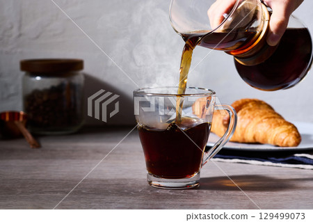 A breakfast scene with croissants and hot coffee poured in. A cafe-style image with white walls and a wooden table. 129499073