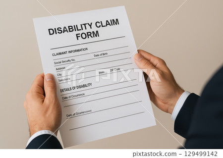Disability claim form held by person wearing dark suit, showing claimant information and details of disability sections on white paper with clear text 129499142