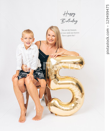 Happy mom and her 5-year-old son pose with a gold number 5 balloon in a studio birthday shoot Happy mom and her 5-year-old son pose with a gold number 5 balloon in a studio birthday shoot 129499475
