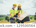 Two men in construction gear are looking at  blueprint 129500564