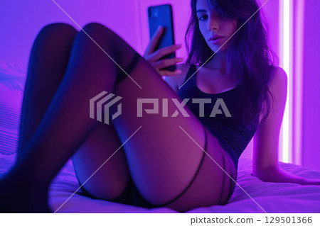 beautiful sexy young woman webcam model in sexual lingerie chats and sexting on mobile smartphone on the bed in the bedroom 129501366