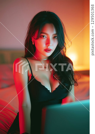 Beautiful sexy young Asian girl webcam model in lingerie chats and sexting online on laptop sitting on bed in bedroom 129501368