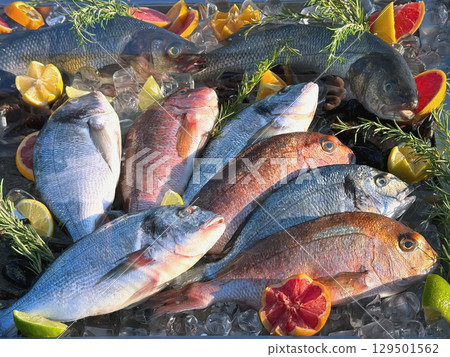 Assortment of fresh fish arranged on ice with citrus slices, rosemary sprigs for display. Open showcases of seafood market. Concept of seafood freshness, gourmet cooking, premium ingredients 129501562