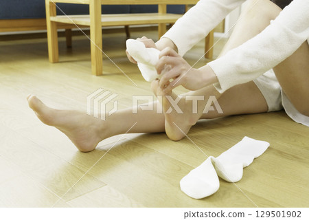 特寫鏡頭:一位年輕女子坐在客廳地板上穿著襪子 特寫鏡頭:一位年輕女子坐在客廳地板上穿著襪子 129501902