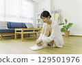 一位年輕女子坐在客廳的地板上，摸著自己的襪子 129501976
