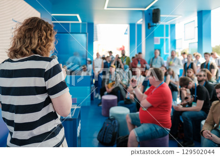 Speaker addressing audience at tech event in modern blue conference space 129502044