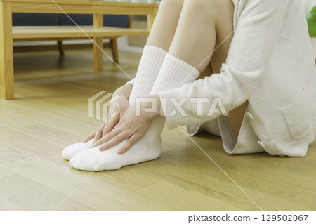 特寫鏡頭：一位年輕女子坐在客廳的地板上烤腳 129502067