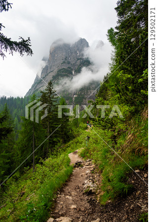 Mountain trail in the Dolomites (Dolomiti, Dolomiten), Italy, leading to Lago Sorapis. The path winds along rocky slopes with stunning views of valleys, forests, and peaks Mountain trail in the Dolomites (Dolomiti, Dolomiten), Italy, leading to Lago Sorapis. The path winds along rocky slopes with stunning views of valleys, forests, and peaks 129502171