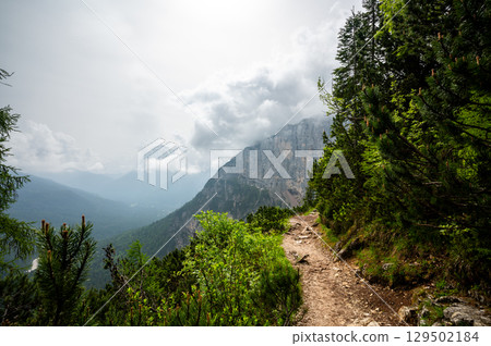Mountain trail in the Dolomites (Dolomiti, Dolomiten), Italy, leading to Lago Sorapis. The path winds along rocky slopes with stunning views of valleys, forests, and peaks Mountain trail in the Dolomites (Dolomiti, Dolomiten), Italy, leading to Lago Sorapis. The path winds along rocky slopes with stunning views of valleys, forests, and peaks 129502184
