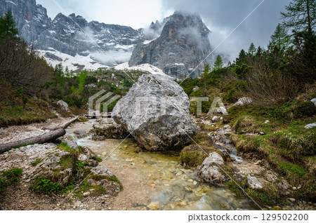 Rocky hiking trail near Lago Sorapis in the Dolomites (Dolomiti, Dolomiten), Italy. The path runs alongside a small mountain stream, with massive boulders and peaks in the background 129502200