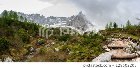 Rocky hiking trail near Lago Sorapis in the Dolomites (Dolomiti, Dolomiten), Italy. The path runs alongside a small mountain stream, with massive boulders and peaks in the background Rocky hiking trail near Lago Sorapis in the Dolomites (Dolomiti, Dolomiten), Italy. The path runs alongside a small mountain stream, with massive boulders and peaks in the background 129502203