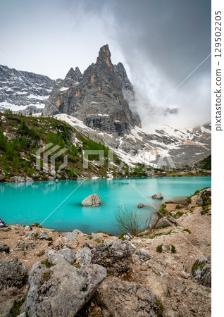 Panoramic view of Lago Sorapis in the Dolomites (Dolomiti, Dolomiten), Italy. The turquoise lake is surrounded by towering cliffs and mountains, a popular spot for hikers and nature lovers 129502205