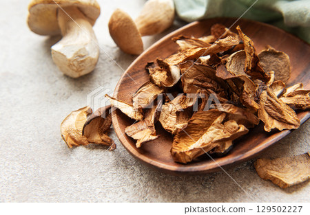 Dried porcini mushrooms resting in wooden bowl on gray textured background 129502227