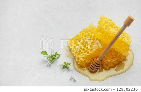 Honeycombs with wooden honey dipper and small white flowers on light background Honeycombs with wooden honey dipper and small white flowers on light background 129502230