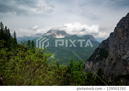 Breathtaking view of forests, mountains, and valleys in the Italian Dolomites (Dolomiti, Dolomiten). Captured from a scenic trail along a rocky ledge. Stunning alpine nature 129502292