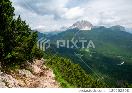 Breathtaking view of forests, mountains, and valleys in the Italian Dolomites (Dolomiti, Dolomiten). Captured from a scenic trail along a rocky ledge. Stunning alpine nature 129502298