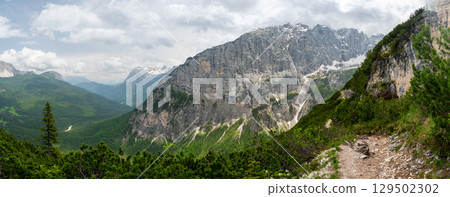 Breathtaking view of forests, mountains, and valleys in the Italian Dolomites (Dolomiti, Dolomiten). Captured from a scenic trail along a rocky ledge. Stunning alpine nature 129502302