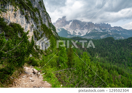 Breathtaking view of forests, mountains, and valleys in the Italian Dolomites (Dolomiti, Dolomiten). Captured from a scenic trail along a rocky ledge. Stunning alpine nature 129502304