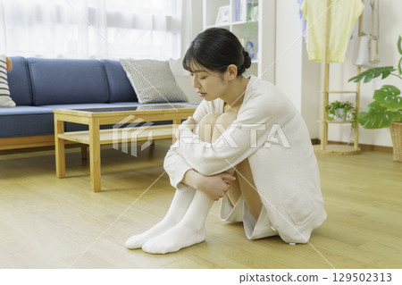 一位年輕女子坐在客廳的地板上，摸著自己的襪子 129502313