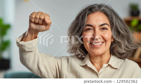 Middle aged latin american woman with raised fist of empowerment, strength and women solidarity, International Womens Day concept 129502362