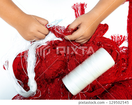 The process of knitting a fishing net. Child hands knitting red yarn with white thread spool on white background 129502545