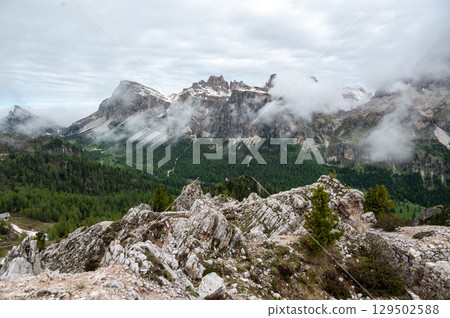 Mountain peaks around Cinque Torri in the Dolomites (Dolomiti, Dolomiten), Italy. Majestic summits partially covered in mist and clouds, with lush forests in the valleys below 129502588