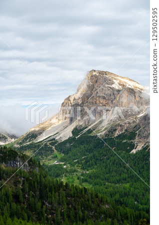 Mountain peaks around Cinque Torri in the Dolomites (Dolomiti, Dolomiten), Italy. Majestic summits partially covered in mist and clouds, with lush forests in the valleys below Mountain peaks around Cinque Torri in the Dolomites (Dolomiti, Dolomiten), Italy. Majestic summits partially covered in mist and clouds, with lush forests in the valleys below 129502595