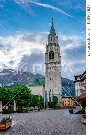 The Basilica Minore dei Santi Filippo e Giacomo in Cortina d'Ampezzo during sunset. Dramatic clouds in the background create a stunning contrast with the church's silhouette 129502625