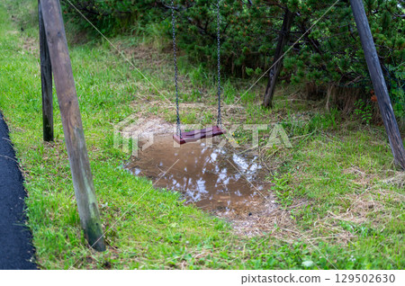 A wooden swing suspended above a water puddle, reflecting the serene atmosphere of nature. A peaceful and nostalgic scene that invites relaxation and contemplation A wooden swing suspended above a water puddle, reflecting the serene atmosphere of nature. A peaceful and nostalgic scene that invites relaxation and contemplation 129502630