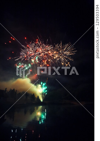 Colorful fireworks illuminate the night sky over a tranquil lake during a summer celebration 129503394