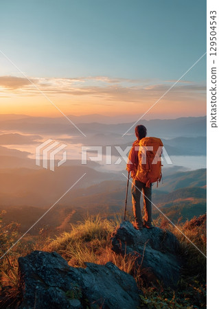 Backpacker standing on mountain top at sunrise with scenic view 129504543