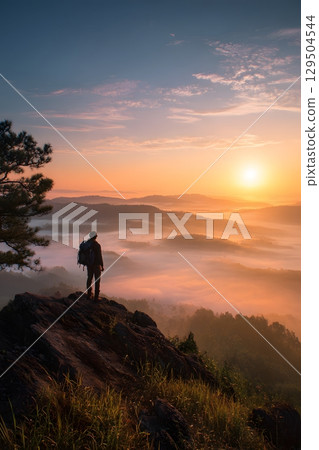 Backpacker standing on mountain top at sunrise with scenic view 129504544