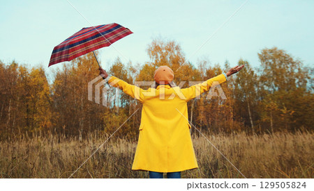 Happy woman in autumn park with umbrella, enjoying warm weather, wearing yellow jacket Happy woman in autumn park with umbrella, enjoying warm weather, wearing yellow jacket 129505824