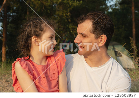 Father and daughter smiling together outdoors in evening sun 129508957