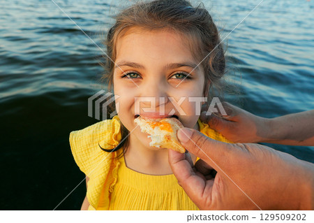 little girl eats pizza close up from daddy's hands against backdrop of sea little girl eats pizza close up from daddy's hands against backdrop of sea 129509202