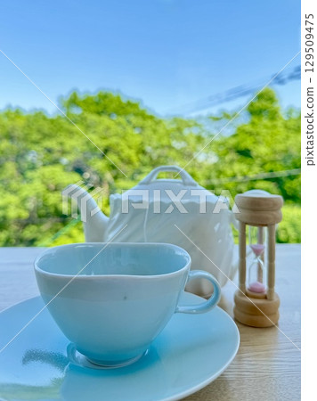 陽光明媚的日子,露台座位上的茶具和沙漏 陽光明媚的日子,露台座位上的茶具和沙漏 129509475