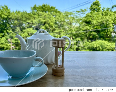 陽光明媚的日子,露台座位上的茶具和沙漏 陽光明媚的日子,露台座位上的茶具和沙漏 129509476