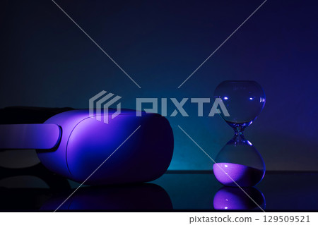 Creative composition featuring a glowing VR headset paired with an hourglass, symbolizing technology and time, on a textured blue backdrop. Perfect for tech, innovation, and timeless concept themes. Creative composition featuring a glowing VR headset paired with an hourglass, symbolizing technology and time, on a textured blue backdrop. Perfect for tech, innovation, and timeless concept themes. 129509521