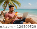A happy man drinks cocktail, watching laptop by the sea. 129509529