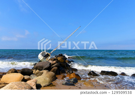 Wide sandy shore under blue sky, wrecked yacht beyond waves. 129509538