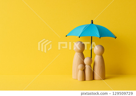 Wooden family figurines positioned under a small blue umbrella on yellow background representing safety and protection 129509729