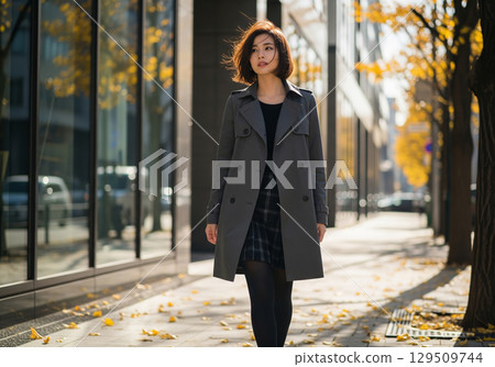 秋裝：一位身穿灰色風衣、短髮飄揚的女模特兒走在城市黃葉林立的道路上 129509744
