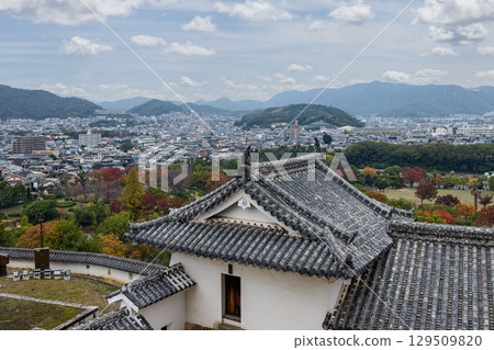 View from Himeji Castle tiled rooftop over colorful autumn park and dense cityscape 129509820