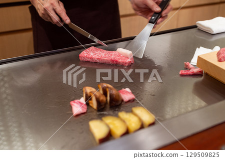 Chef slicing A5 Kobe beef on a hot teppanyaki grill with shiitake mushrooms, sweet potato, beef fat Chef slicing A5 Kobe beef on a hot teppanyaki grill with shiitake mushrooms, sweet potato, beef fat 129509825