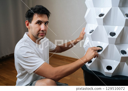 Portrait of gardener male placing rockwool cube inside net pot, inserting it into hydroponic tower system, preparing for seed starting and modern agriculture. Concept of indoor farming. Portrait of gardener male placing rockwool cube inside net pot, inserting it into hydroponic tower system, preparing for seed starting and modern agriculture. Concept of indoor farming. 129510072