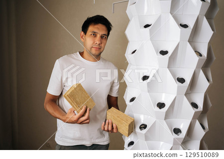 Portrait of professional gardener holding rockwool slabs for seed planting in vertical hydroponic garden, demonstrating sustainable urban agriculture innovation. Concept of indoor farming. 129510089