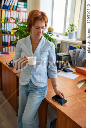 Woman taking a coffee break at her desk in a quiet office setting. Mindful pause, mental reset, and slow work lifestyle. 129510340