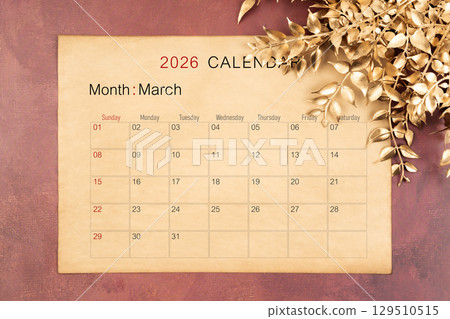 March 2026 calendar page with golden color leaves on red wooden background. 129510515